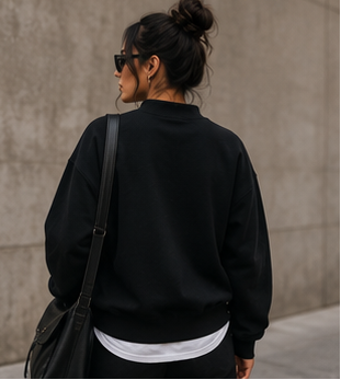 Woman wearing a black 'UNLEASH FAITH' sweatshirt against a concrete wall.