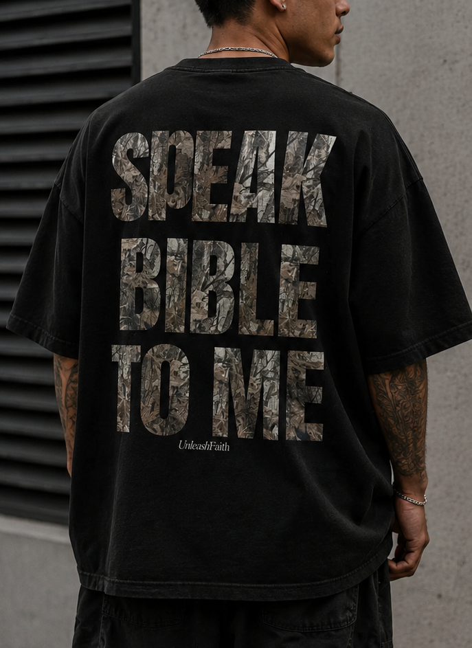 Person wearing a black t-shirt with text, standing against a concrete wall.