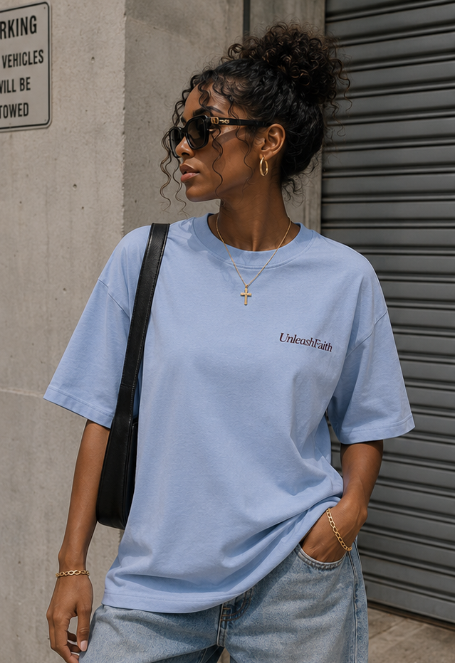 Woman wearing a light blue t-shirt with text, standing against a concrete wall.